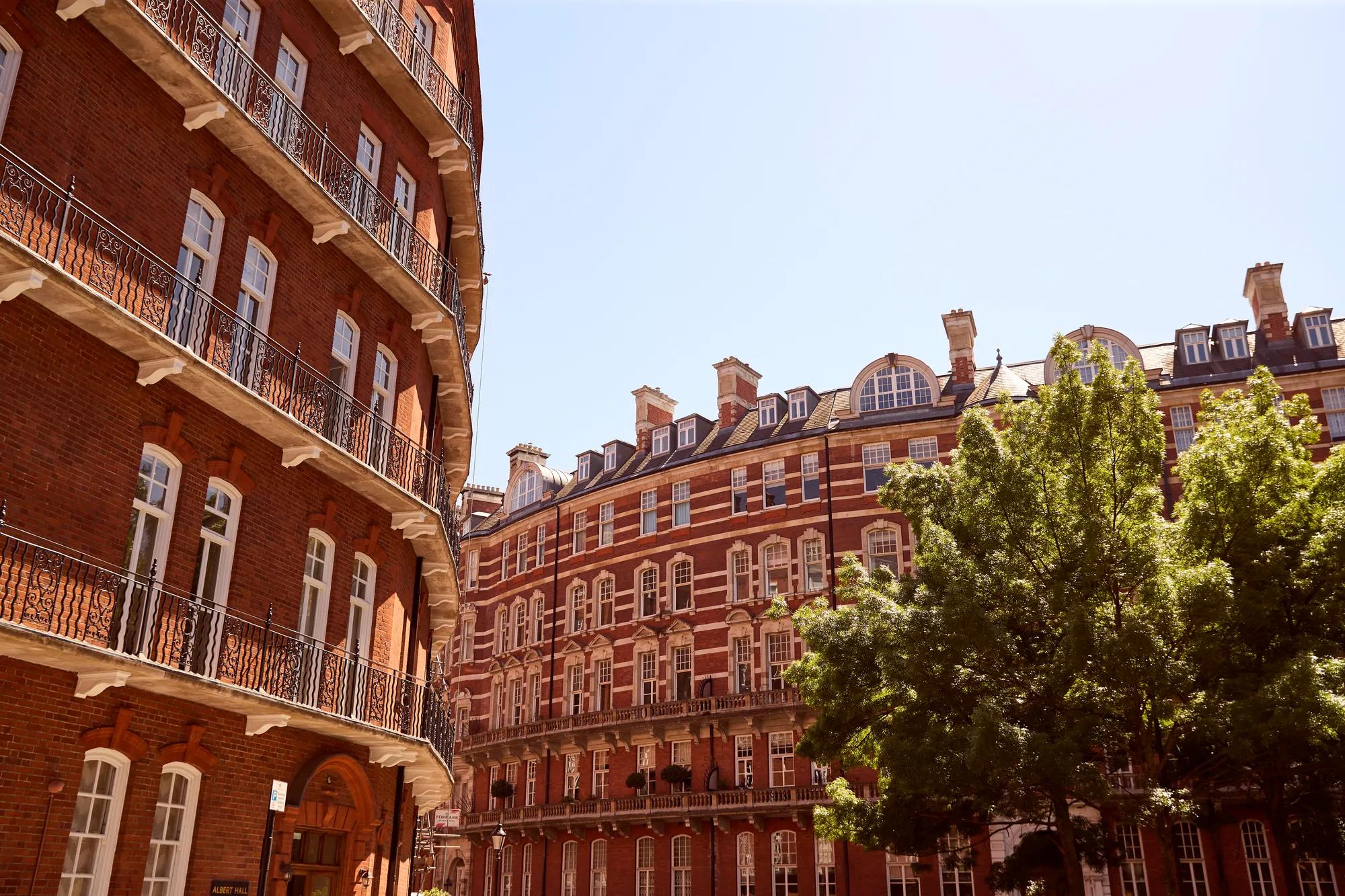 Copilot said:

Red-brick residential buildings with ornate balconies and large windows surrounding a leafy courtyard under a clear blue sky.