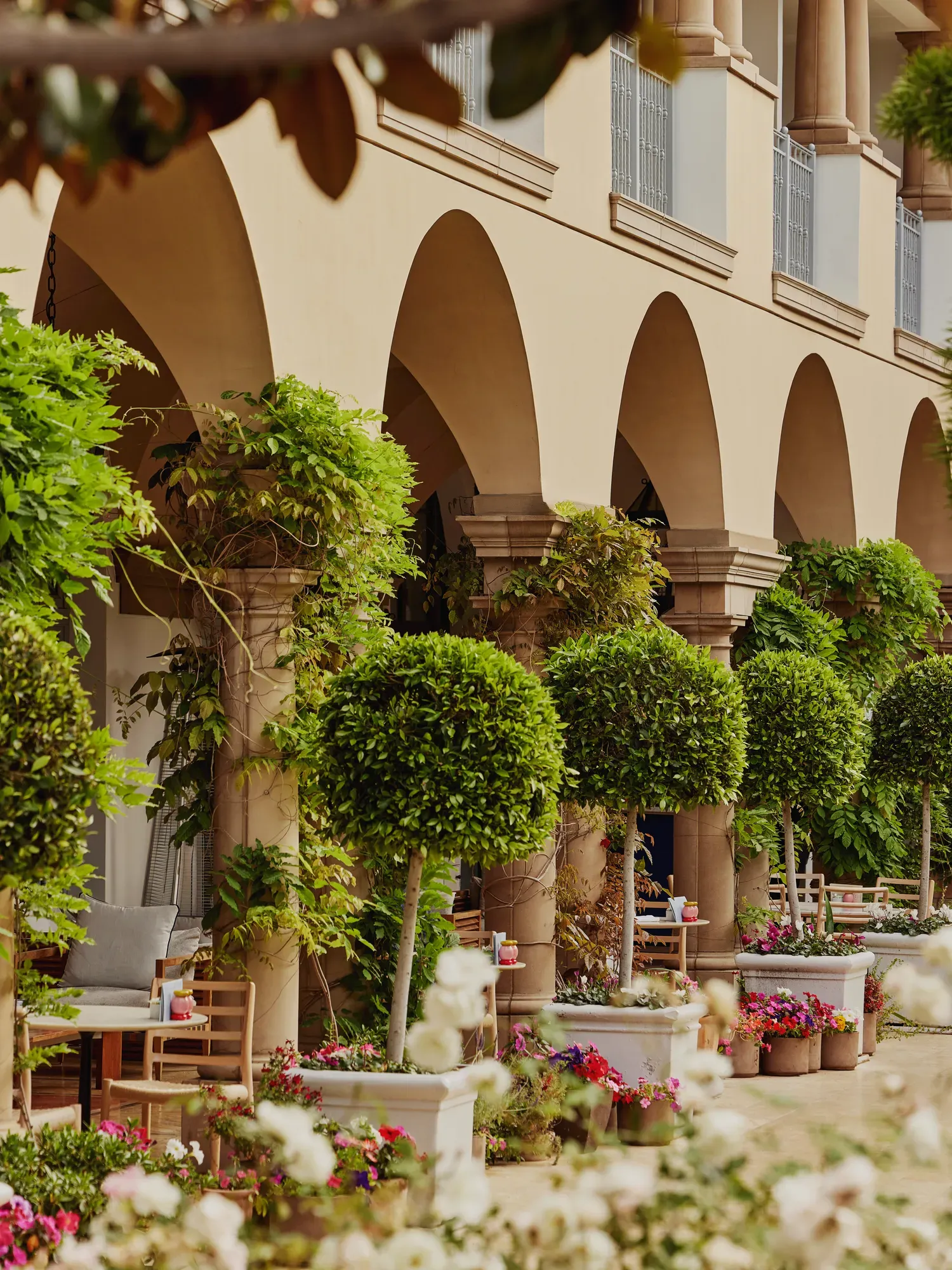 Beverly Canon Garden walkway by Maybourne Café with arched colonnade, potted topiary trees and blooming planters.