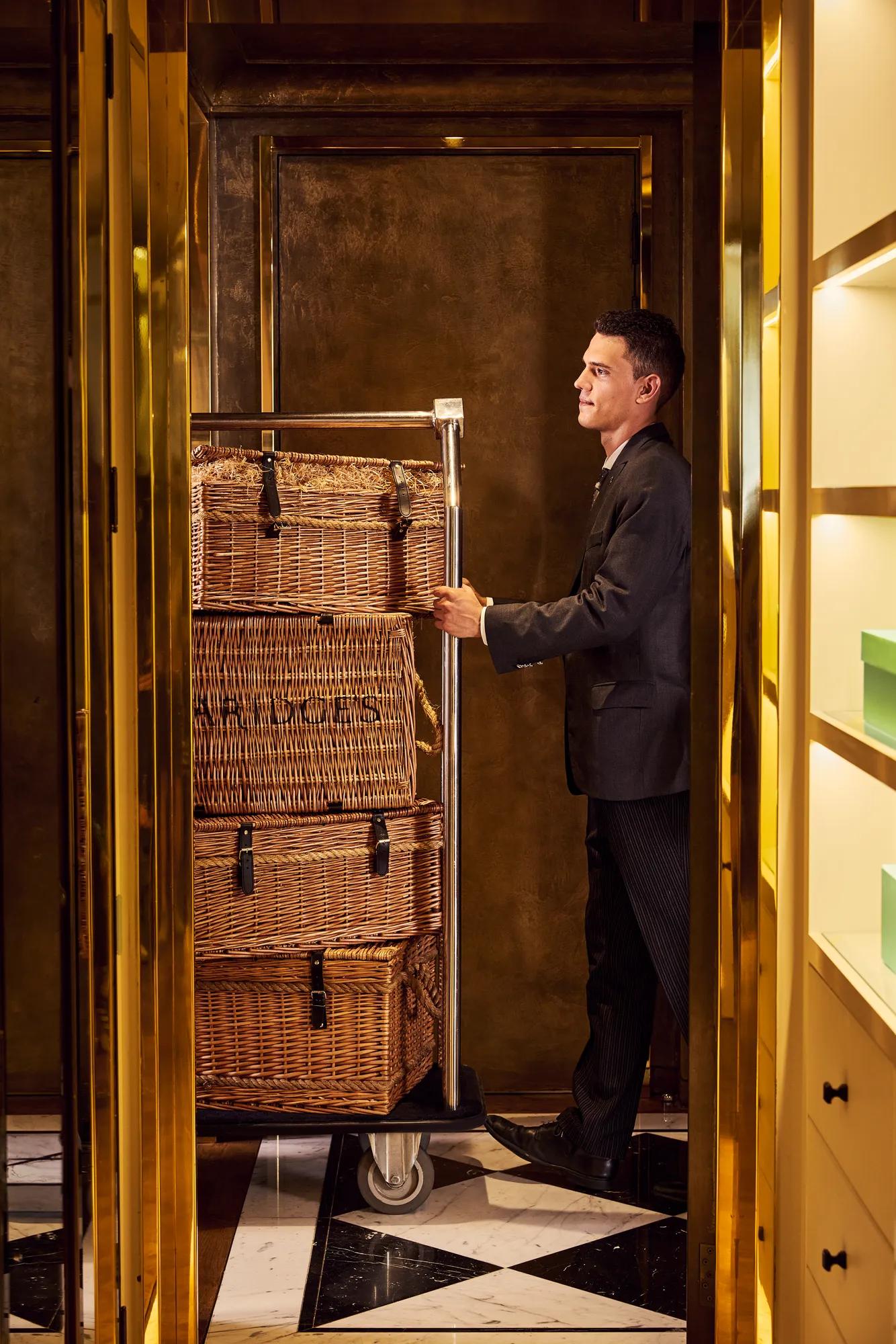 Hotel staff member transporting stacked wicker luggage trunks on a trolley through an elegant hallway.