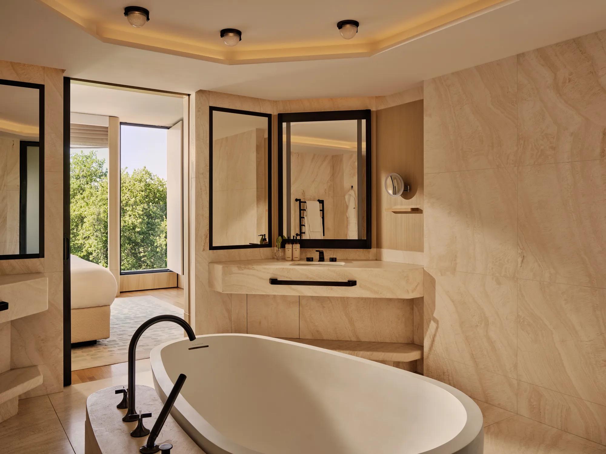 A marble bathroom with a large white tub, mirror and sink