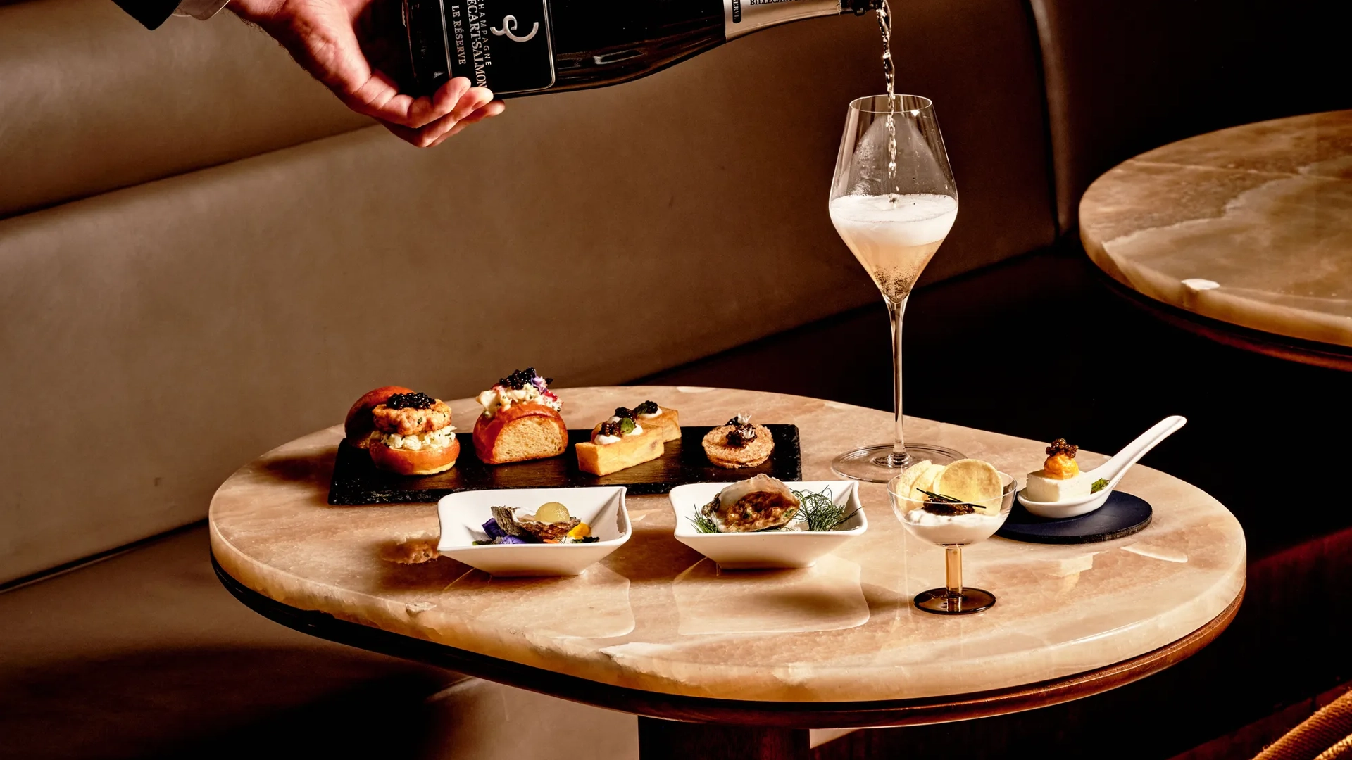 Hand pouring champagne into flute beside gourmet canapés and caviar at Maybourne Beverly Hills