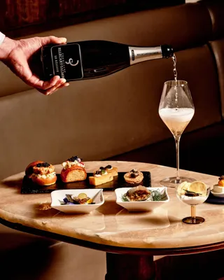 Hand pouring champagne into flute beside gourmet canapés and caviar at Maybourne Beverly Hills