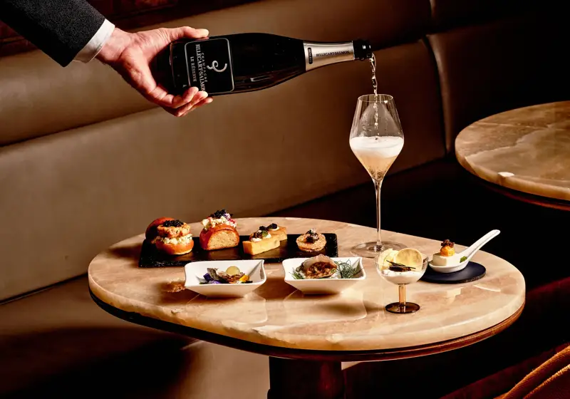 Hand pouring champagne into flute beside gourmet canapés and caviar at Maybourne Beverly Hills