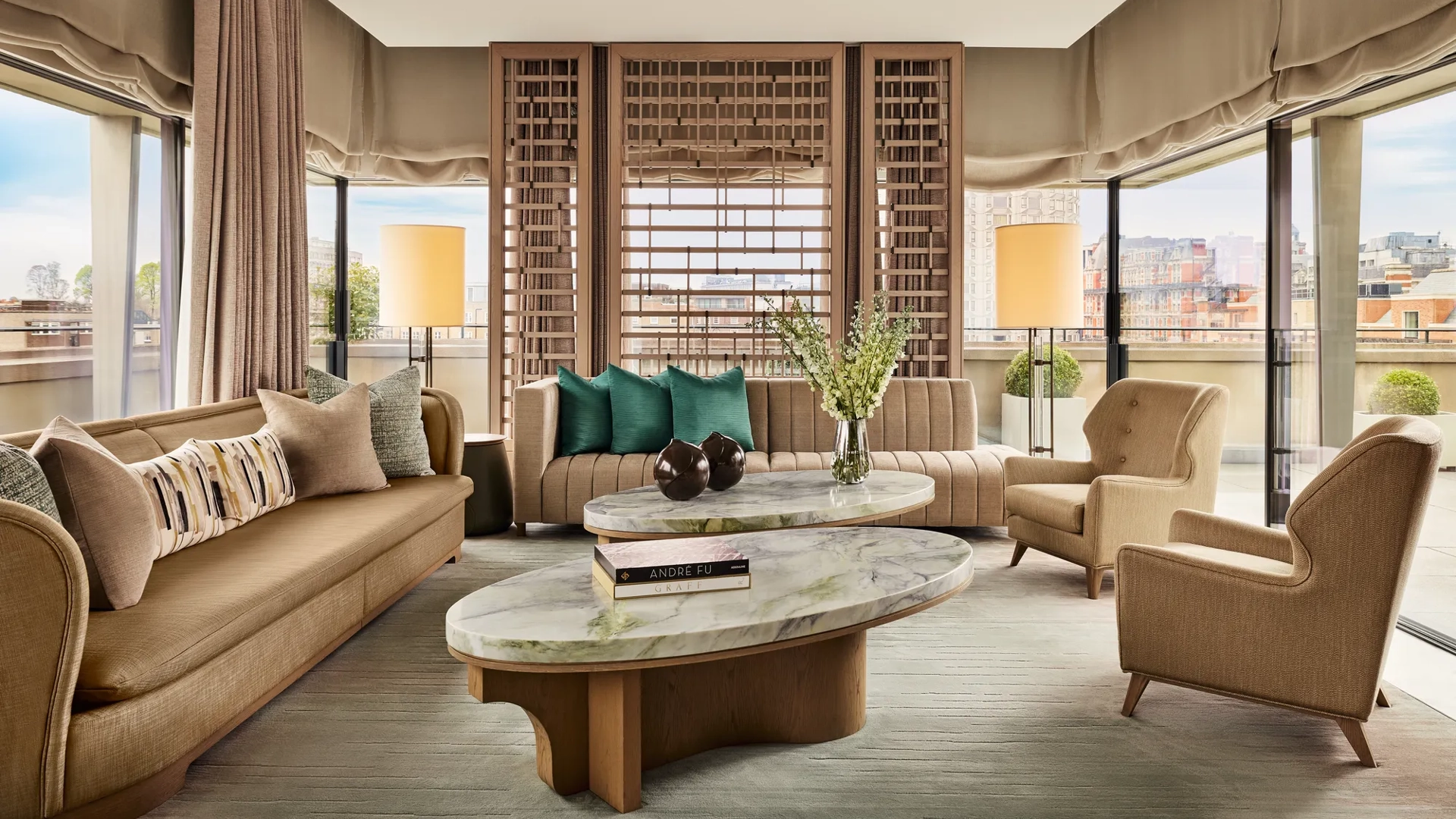 Bright living room with marble coffee tables, neutral sofas, green accent cushions, and city views through floor-to-ceiling windows