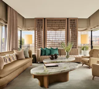 Bright living room with marble coffee tables, neutral sofas, green accent cushions, and city views through floor-to-ceiling windows