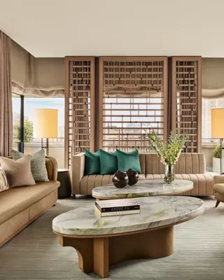 Bright living room with marble coffee tables, neutral sofas, green accent cushions, and city views through floor-to-ceiling windows