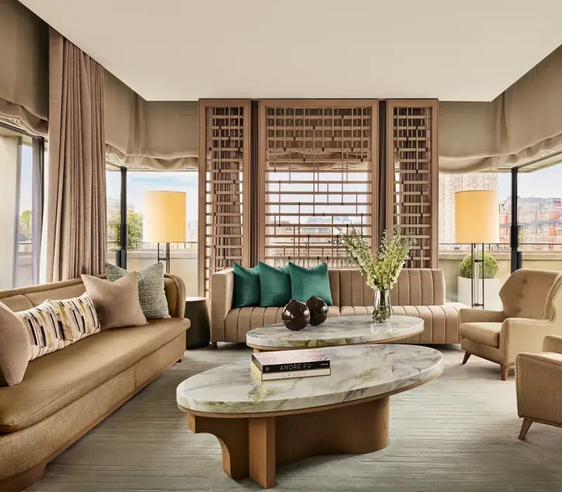 Bright living room with marble coffee tables, neutral sofas, green accent cushions, and city views through floor-to-ceiling windows