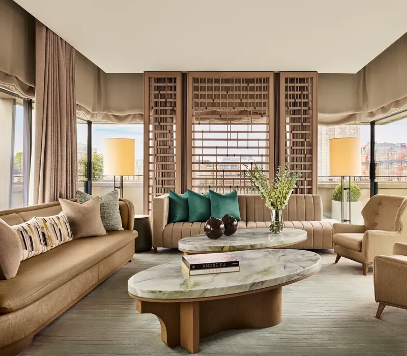 Bright living room with marble coffee tables, neutral sofas, green accent cushions, and city views through floor-to-ceiling windows