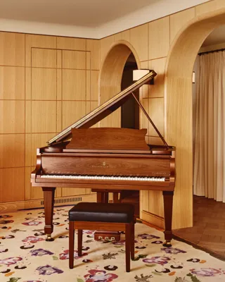 Steinway & Sons grand piano in polished walnut with a black leather stool, set against curved wooden archways and pale wood wall panelling on a floral-patterned rug.