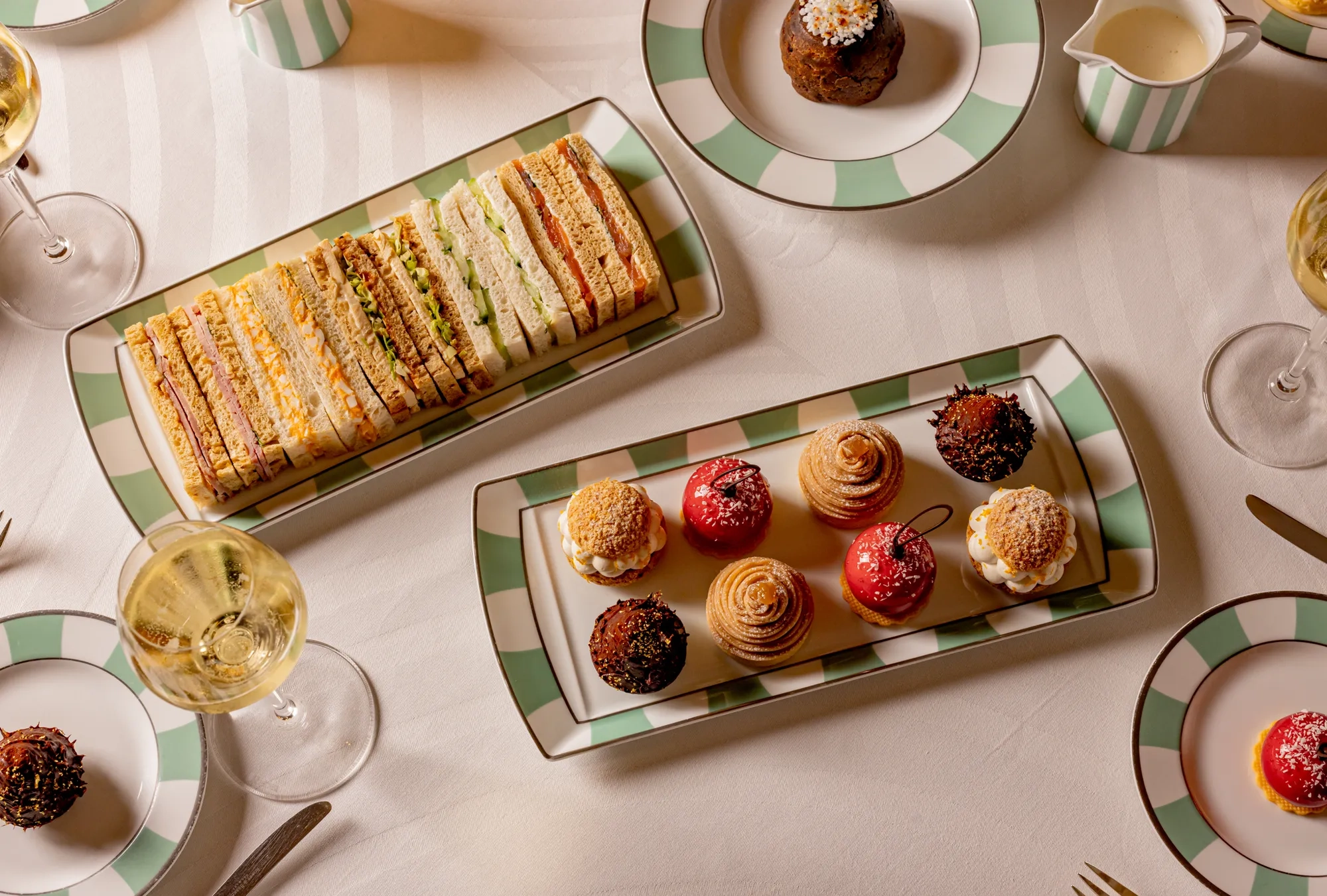 Afternoon tea spread with finger sandwiches, miniature pastries and champagne on striped china.
