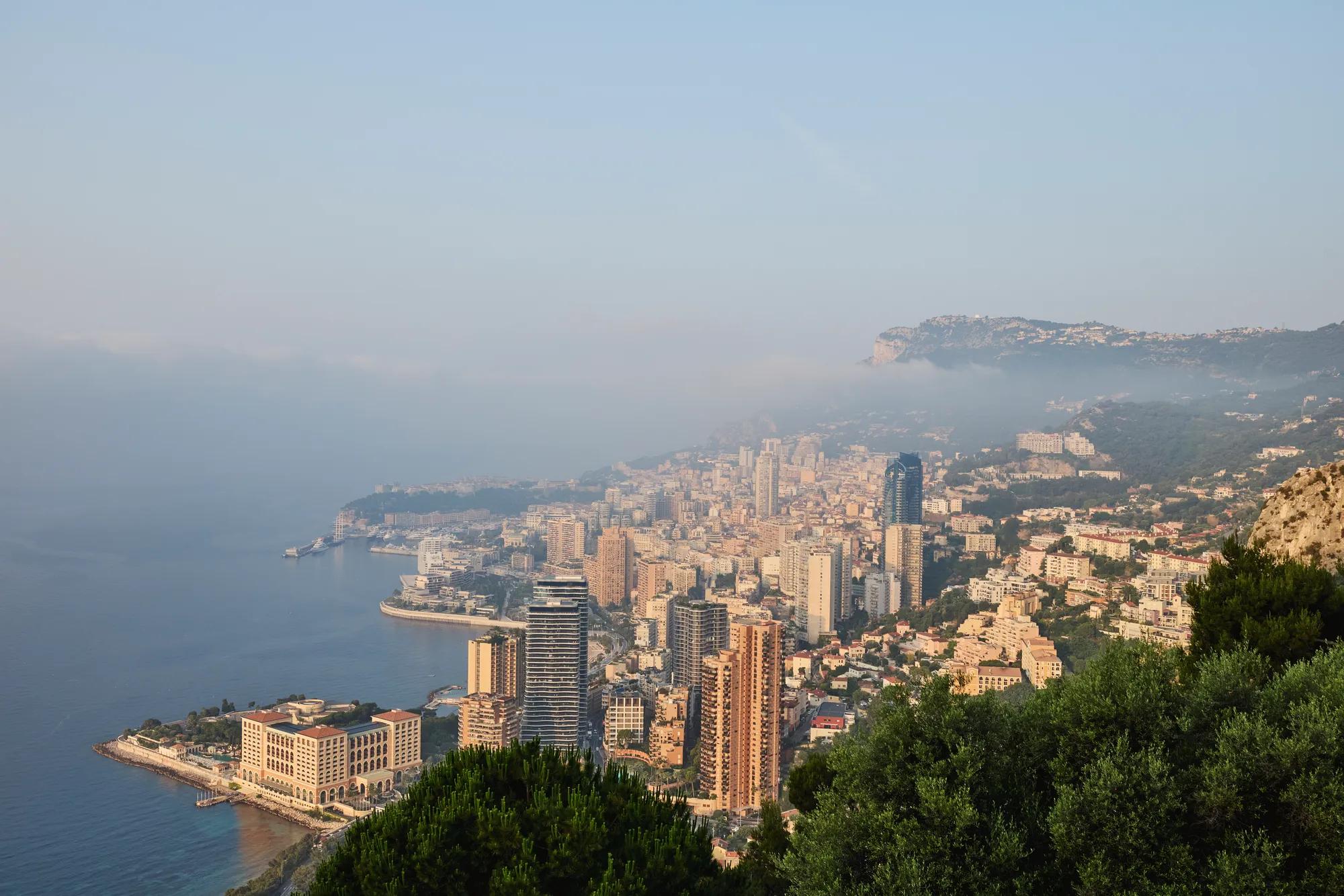 High-angle view of the Riviera coastline with tall buildings by the sea and green hills in soft haze.
