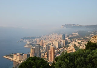 Vue en hauteur de la côte de la Riviera, avec de hauts immeubles au bord de la mer et des collines verdoyantes dans la brume.