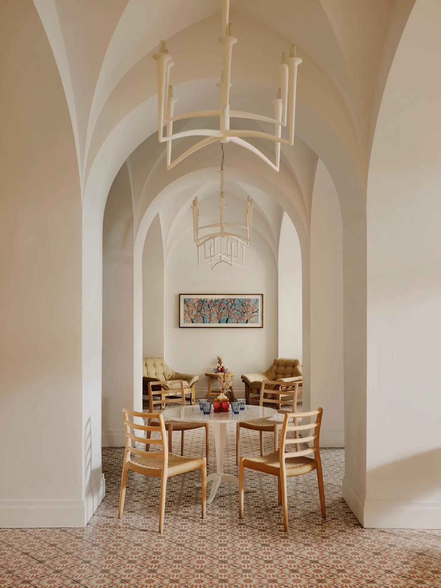 Arched café corridor with chandeliers, small round tables, and a lounge seating area at the far end.