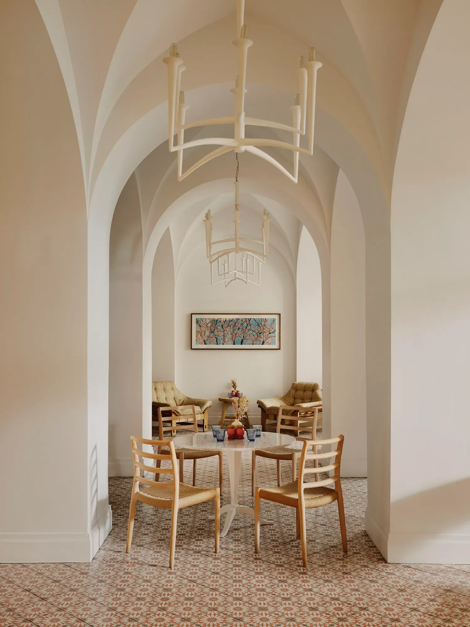 Arched café corridor with chandeliers, small round tables, and a lounge seating area at the far end.