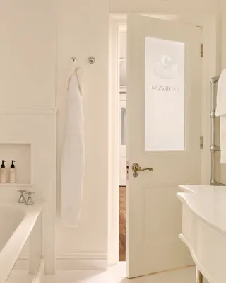 Light, elegant bathroom with a bathtub, white robes, marble sink, and a door etched with “Bathroom.”