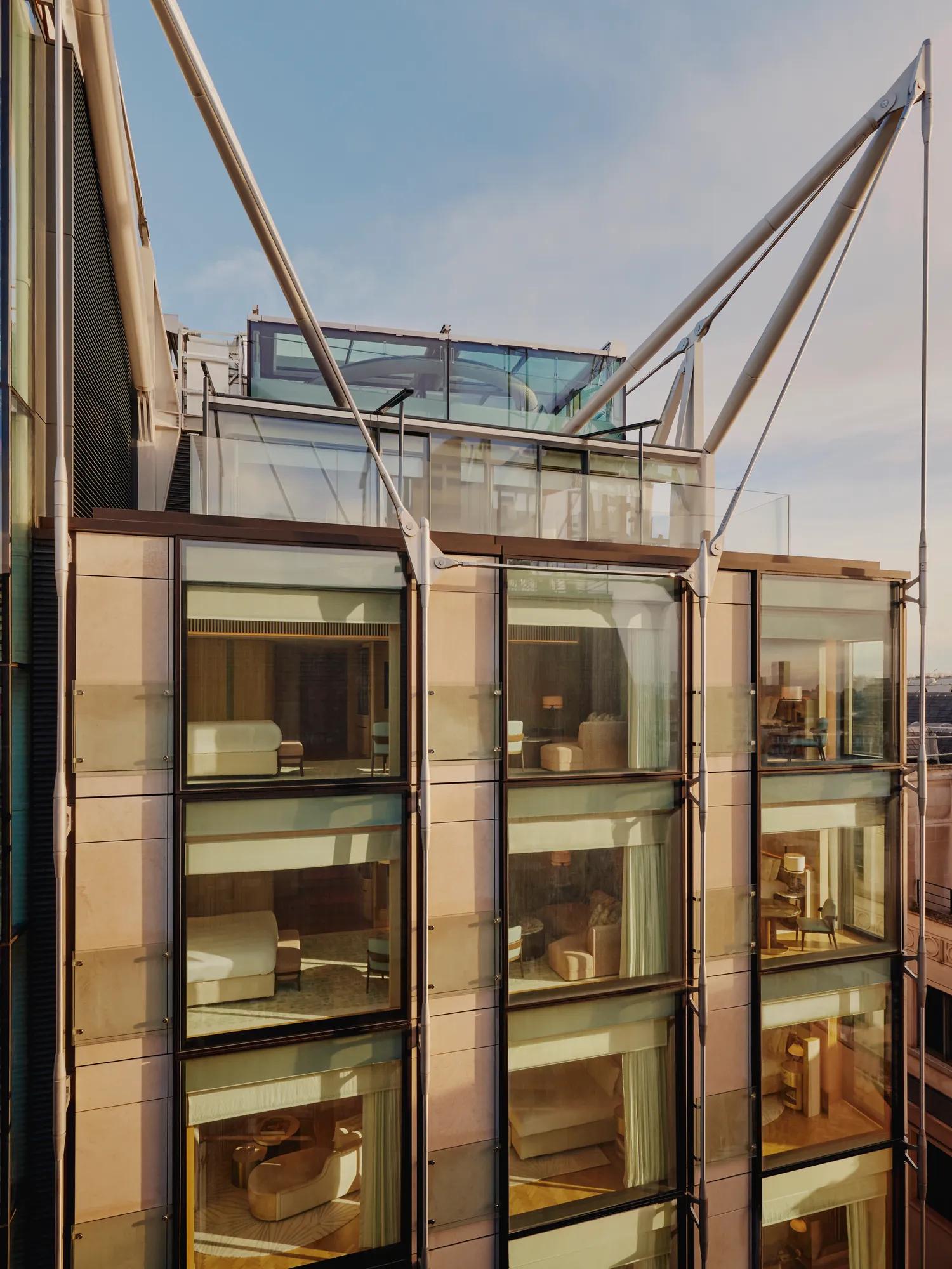 Glass-fronted façade of The Emory showing multiple suite levels, rooftop terrace, and exposed structural supports.