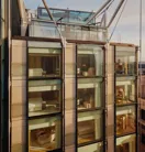 Glass-fronted façade of The Emory showing multiple suite levels, rooftop terrace, and exposed structural supports.