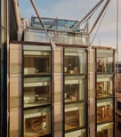 Glass-fronted façade of The Emory showing multiple suite levels, rooftop terrace, and exposed structural supports.