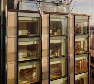 Glass-fronted façade of The Emory showing multiple suite levels, rooftop terrace, and exposed structural supports.