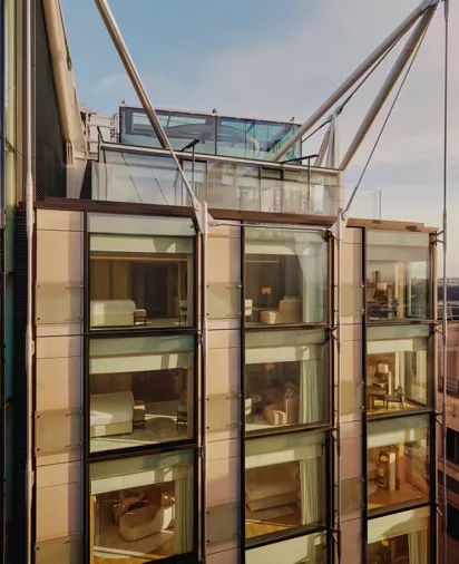 Glass-fronted façade of The Emory showing multiple suite levels, rooftop terrace, and exposed structural supports.