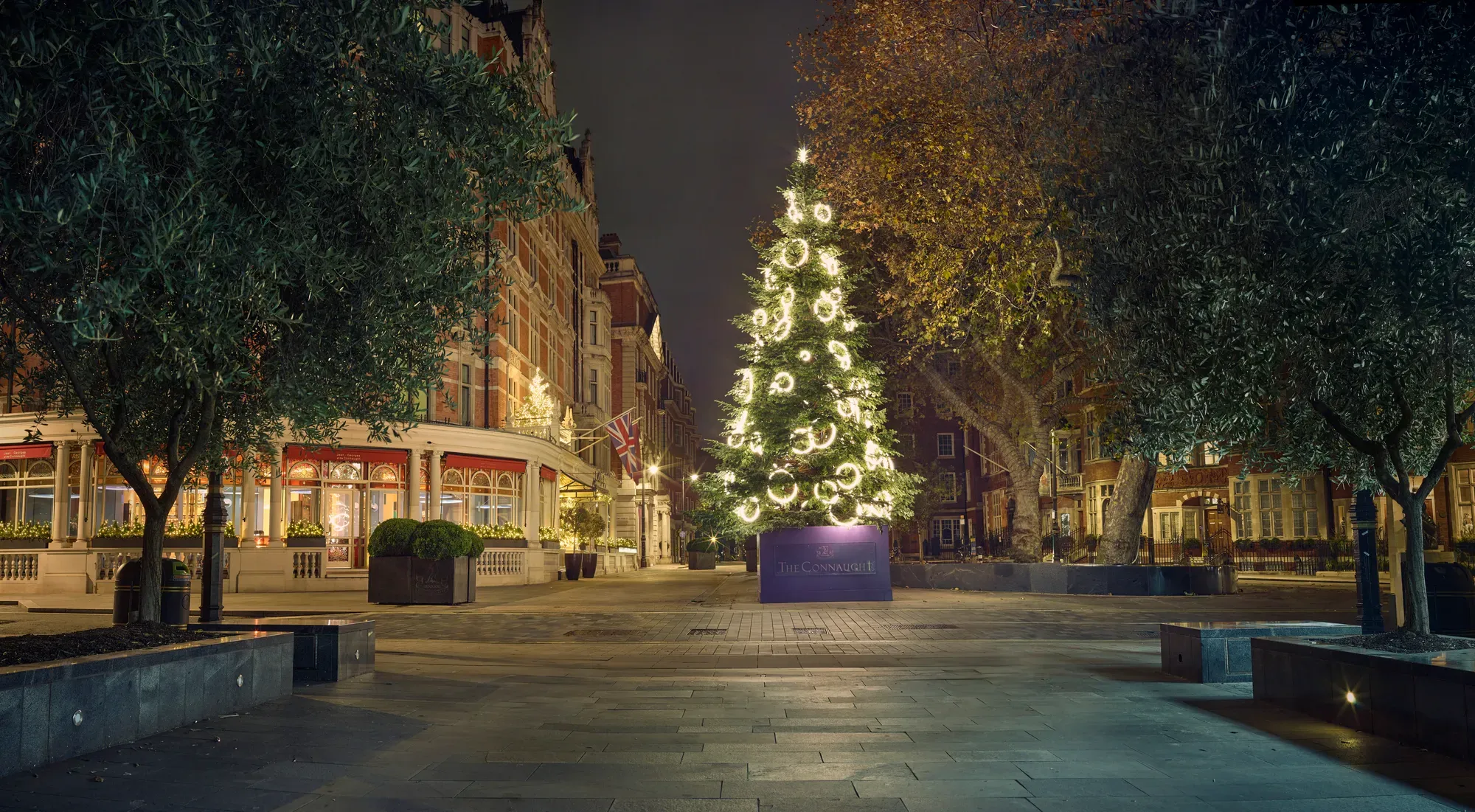 Illuminated Christmas tree in courtyard outside luxury London hotel at night.