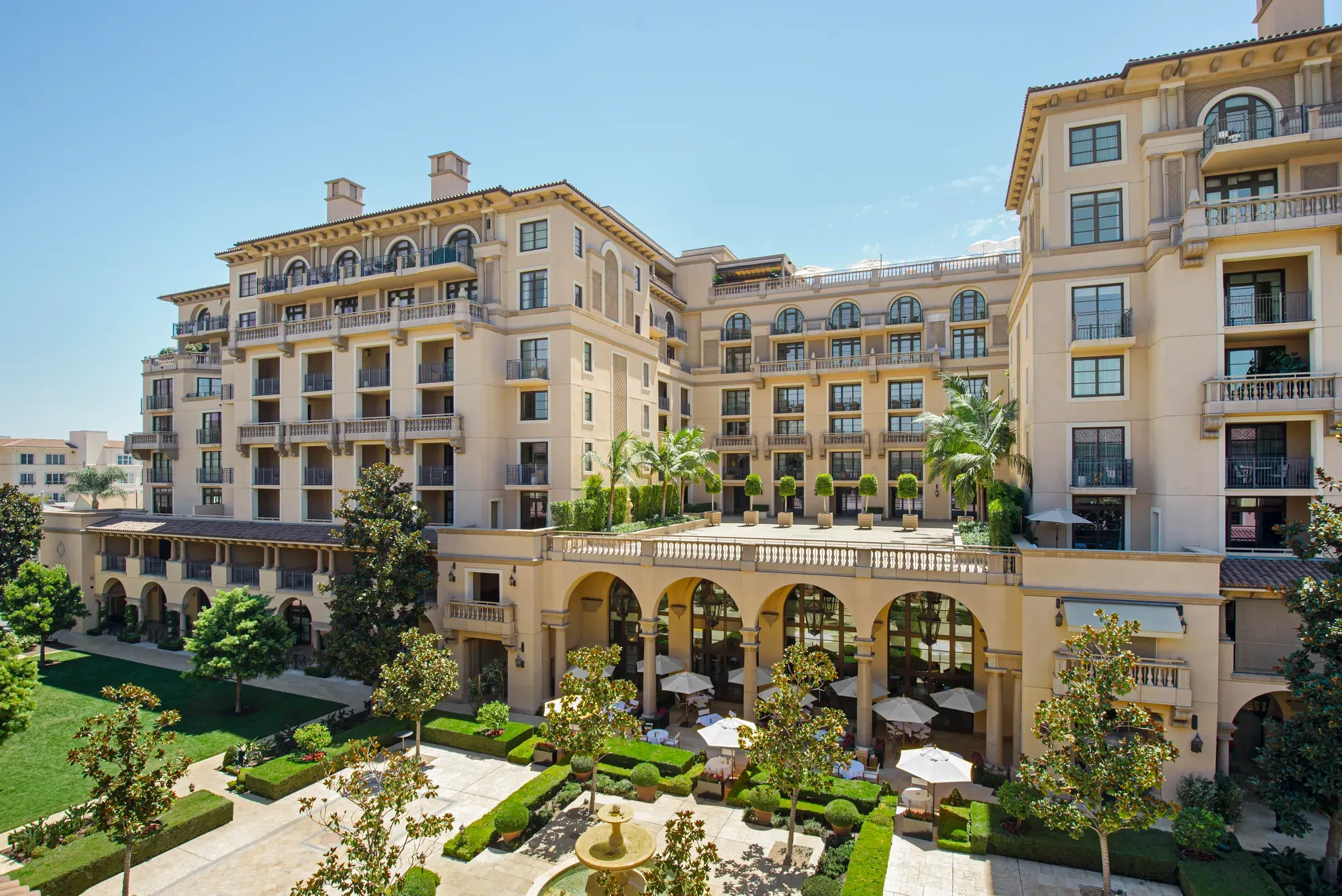 Elevated view of The Maybourne Beverly Hills overlooking Beverly Canon Gardens with arches, balconies, and a central fountain.