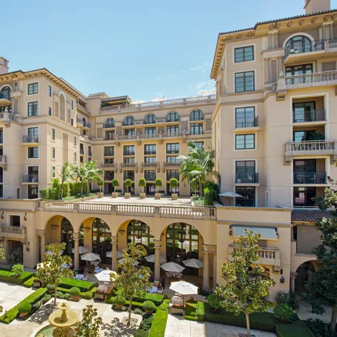 Elevated view of The Maybourne Beverly Hills overlooking Beverly Canon Gardens with arches, balconies, and a central fountain.