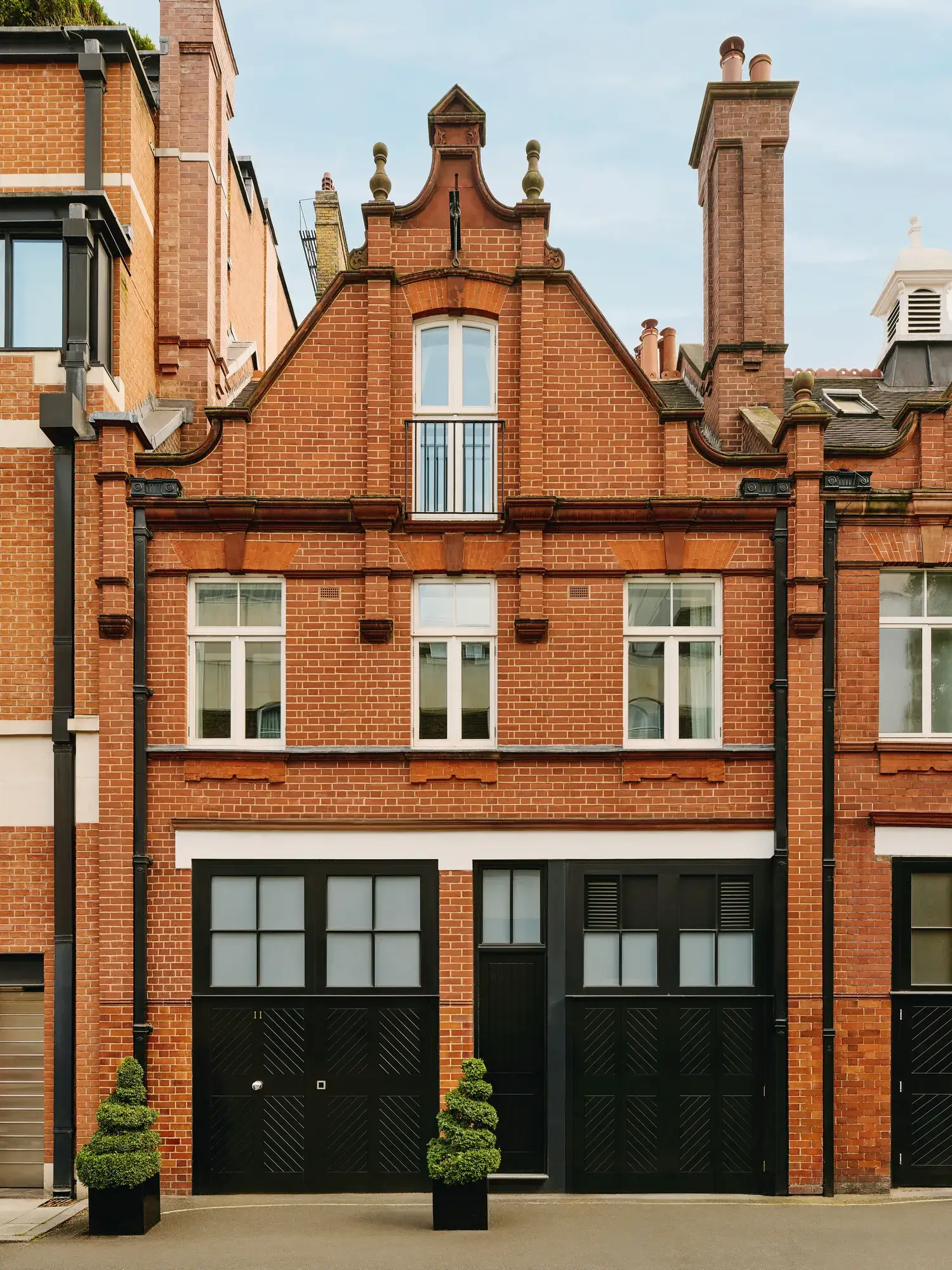 Red-brick townhouse facade with black doors, white-framed windows, and small topiary plants.