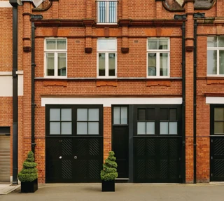Red-brick townhouse facade with black doors, white-framed windows, and small topiary plants.