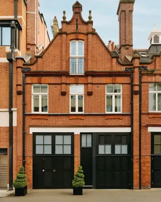 Red-brick townhouse facade with black doors, white-framed windows, and small topiary plants.