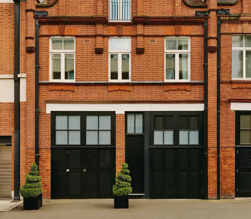 Red-brick townhouse facade with black doors, white-framed windows, and small topiary plants.