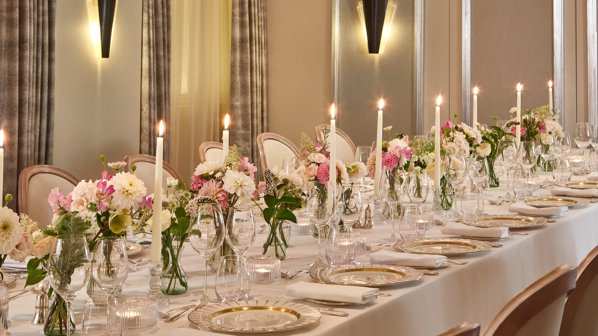 Elegant dining table at Claridge’s set with white linens, crystal glassware, gold-rimmed plates, tall candles, and floral centrepieces in soft pink and white tones.
