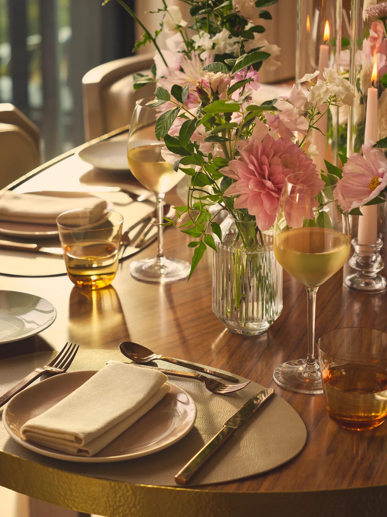 Close-up of table with wine glasses, floral centrepiece, and neatly folded napkins in soft, golden lighting.