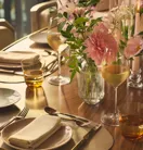Close-up of table with wine glasses, floral centrepiece, and neatly folded napkins in soft, golden lighting.