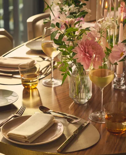 Close-up of table with wine glasses, floral centrepiece, and neatly folded napkins in soft, golden lighting.
