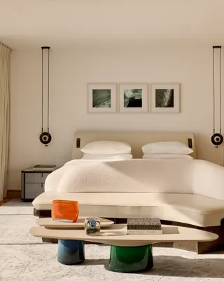 Chambre d’hôtel moderne avec grand lit, banquette incurvée et table basse, dotée de boiseries et de portes vitrées s’ouvrant sur une terrasse.