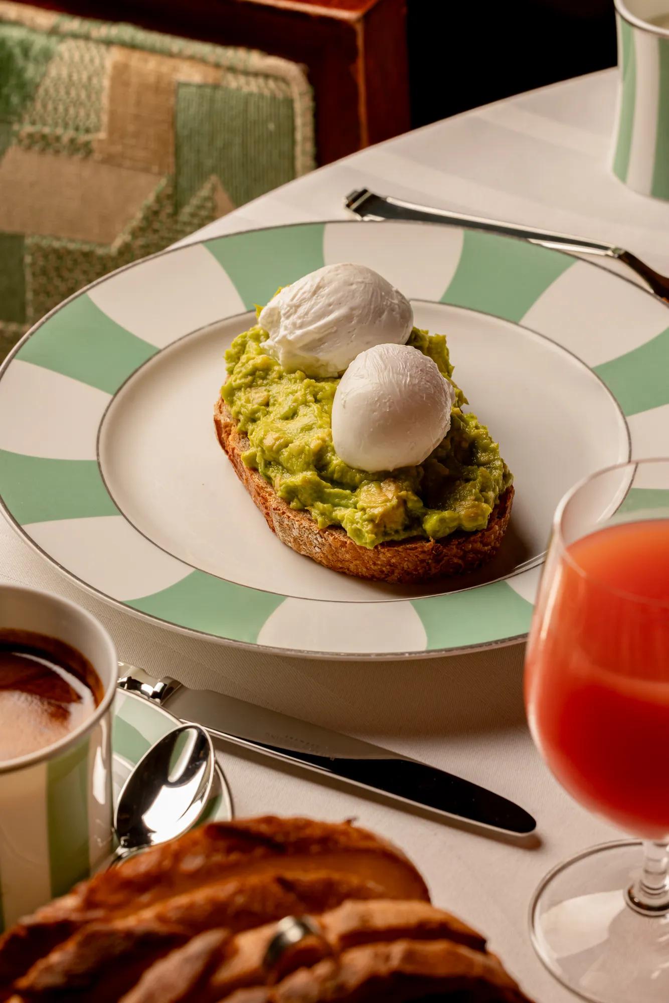 Avocado toast topped with two poached eggs on a striped plate, served with coffee and juice.