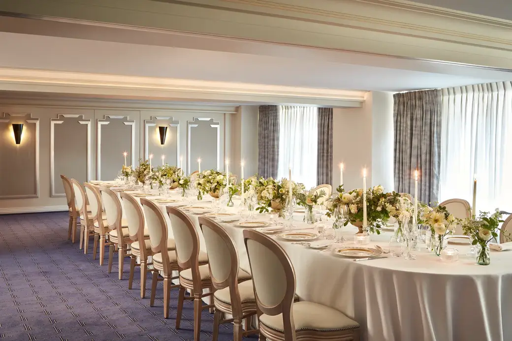 The St James Room at Claridge’s set for a private dinner with an elegant U-shaped table arrangement, white linen, floral centrepieces, and candlelight by the windows.