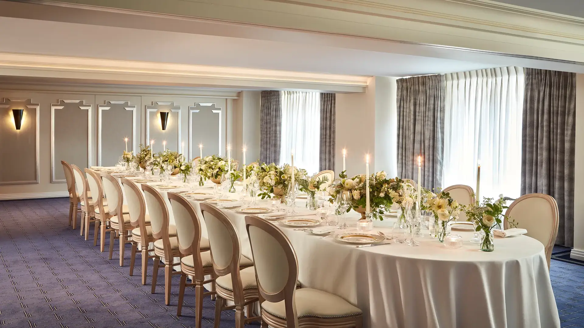 The St James Room at Claridge’s set for a private dinner with an elegant U-shaped table arrangement, white linen, floral centrepieces, and candlelight by the windows.