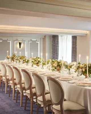 The St James Room at Claridge’s set for a private dinner with an elegant U-shaped table arrangement, white linen, floral centrepieces, and candlelight by the windows.