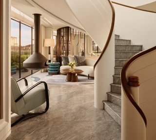 Curved staircase leading to a bright living area with floor-to-ceiling windows, modern furniture, and a suspended fireplace at Claridge’s