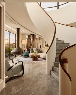 Curved staircase leading to a bright living area with floor-to-ceiling windows, modern furniture, and a suspended fireplace at Claridge’s