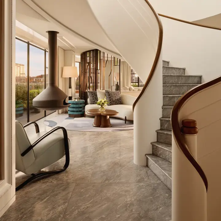 Curved staircase leading to a bright living area with floor-to-ceiling windows, modern furniture, and a suspended fireplace at Claridge’s