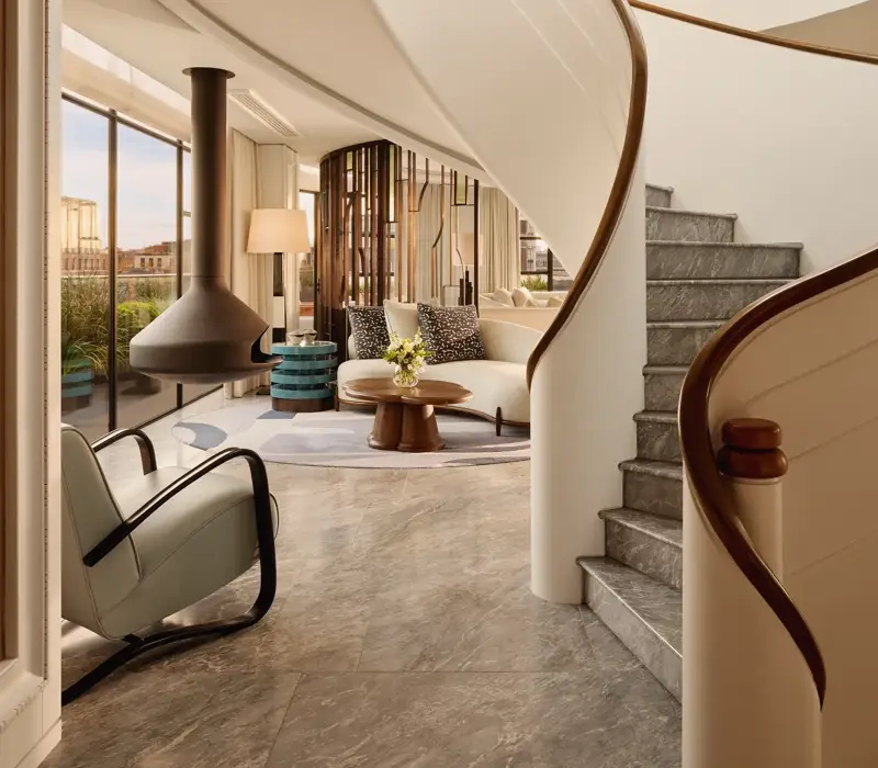 Curved staircase leading to a bright living area with floor-to-ceiling windows, modern furniture, and a suspended fireplace at Claridge’s