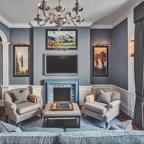 Refined sitting room with grey seating, blue-tiled fireplace, chandelier, and built-in study nook.
