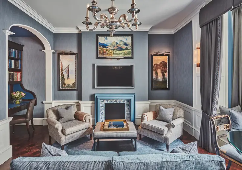 Refined sitting room with grey seating, blue-tiled fireplace, chandelier, and built-in study nook.