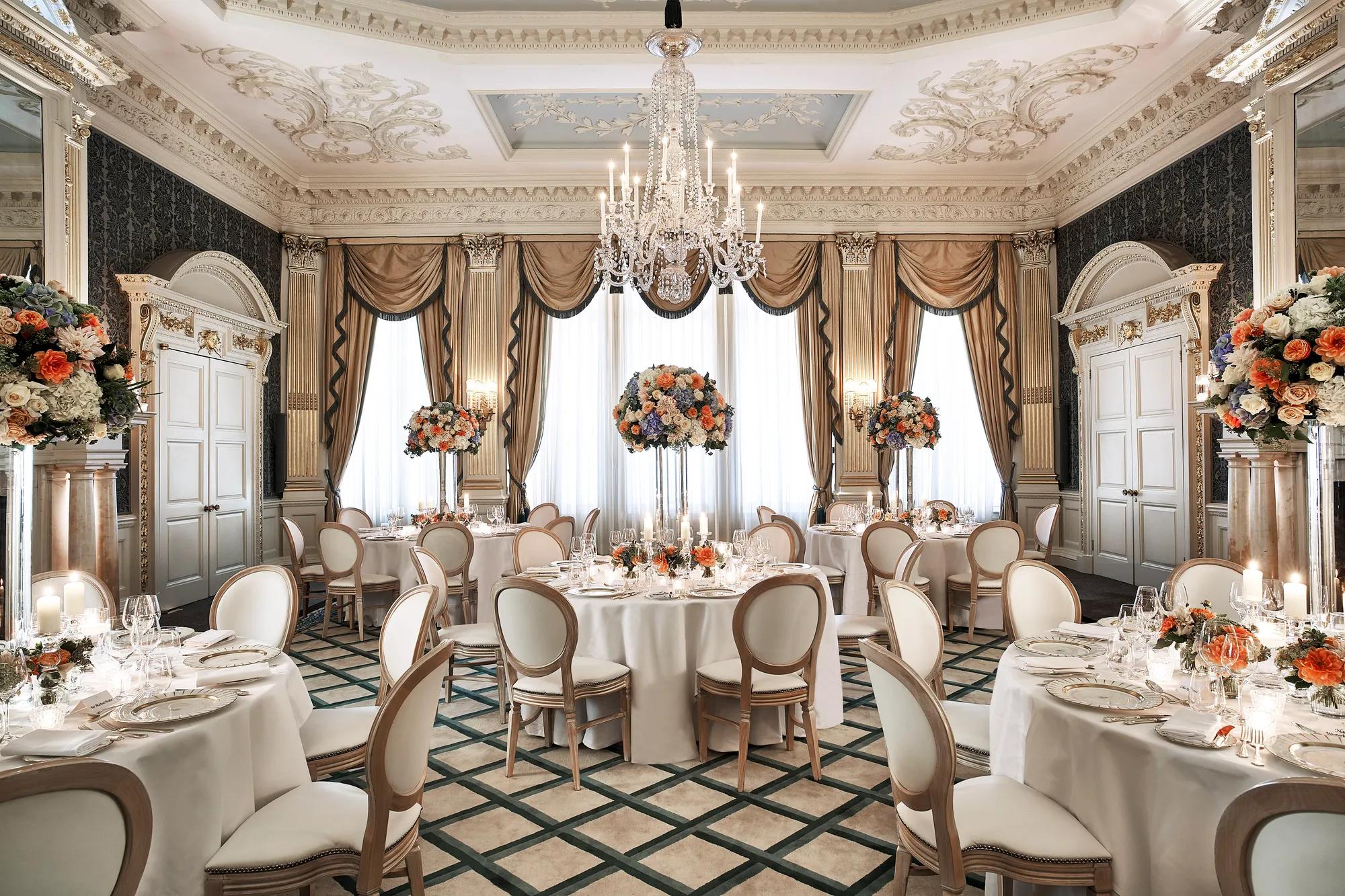 Grand ballroom set for dining with round tables, floral centerpieces, and crystal chandelier.