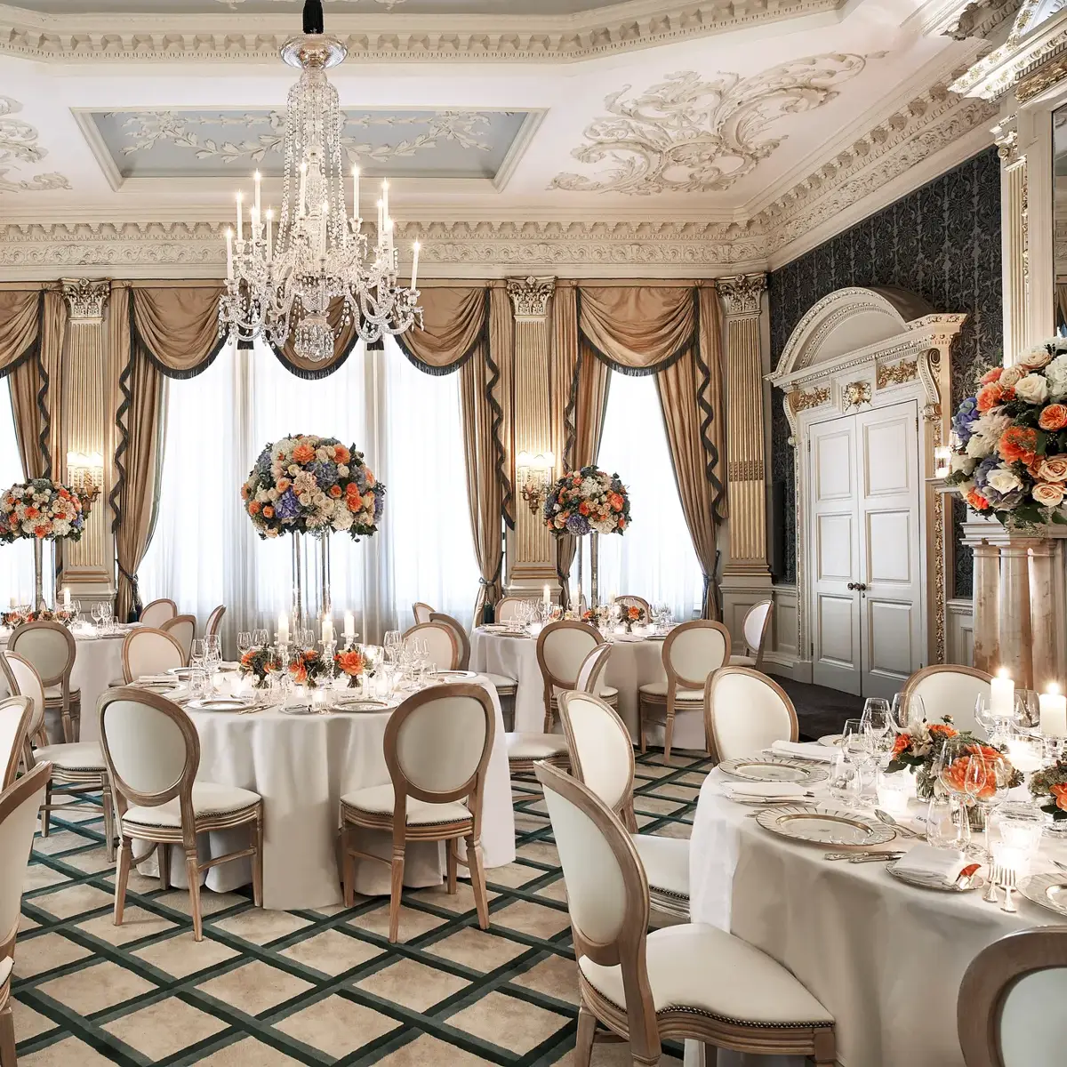 Grand ballroom set for dining with round tables, floral centerpieces, and crystal chandelier.