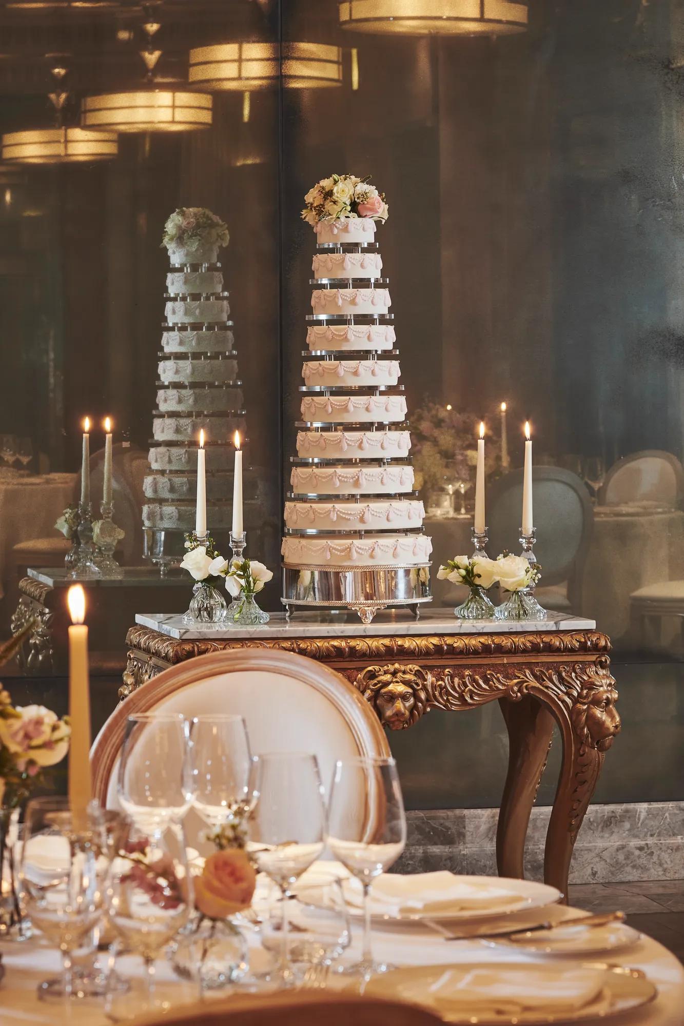 Tall tiered wedding cake displayed on ornate table with candles and floral accents.