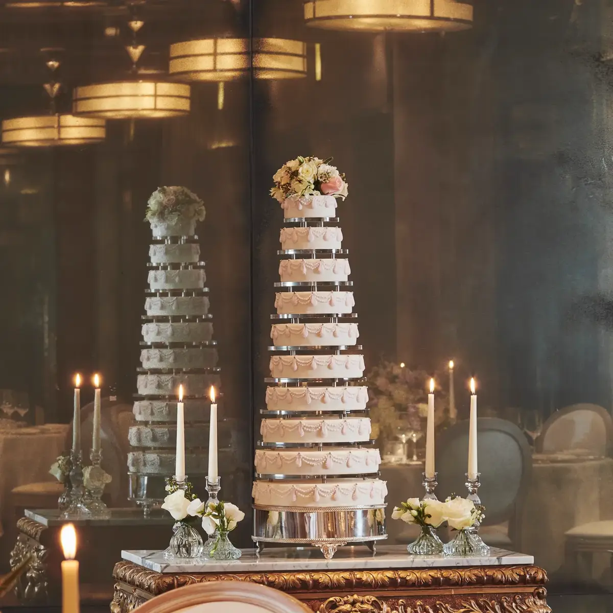 Tall tiered wedding cake displayed on ornate table with candles and floral accents.